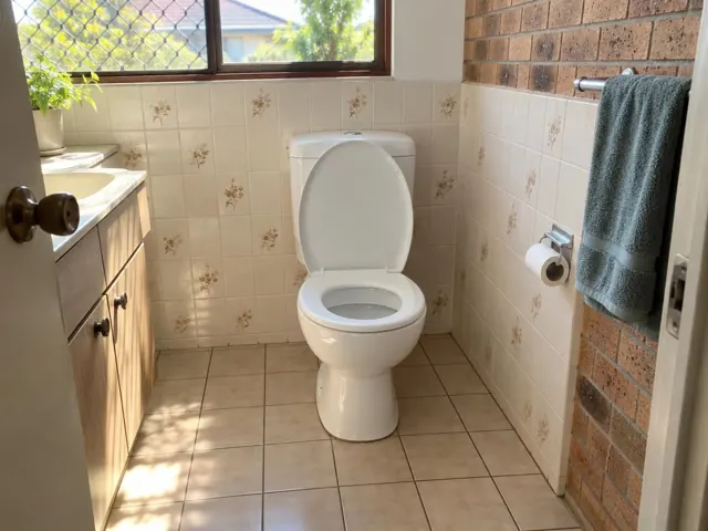 Clean white toilet in a tiled bathroom with brick wall and vanity in Canley Vale