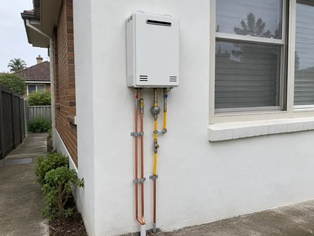 Wall-mounted hot water unit with copper and gas piping beside a house window in Berala