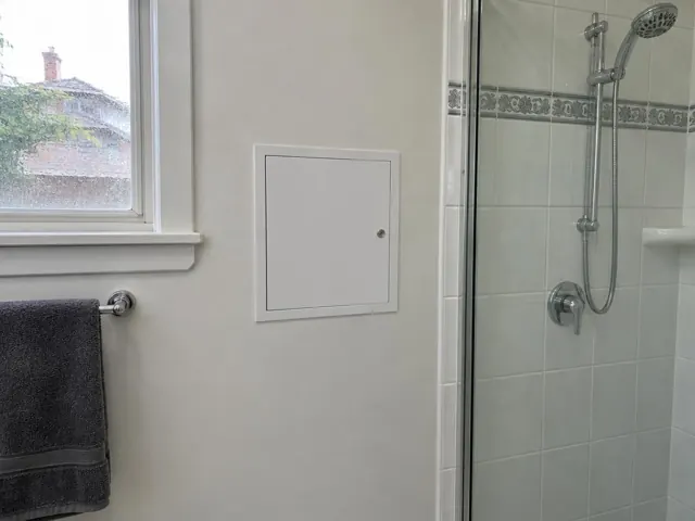 Bathroom wall with a small access panel beside a shower and window in Cabramatta